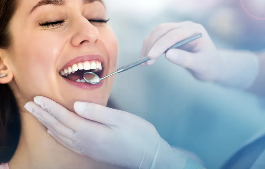 Une femme heureuse recevant un examen dentaire par un dentiste professionnel à Differdange, souriant largement alors qu'elle est examinée avec un miroir dentaire.