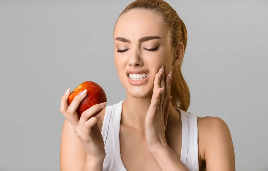 Une jeune femme ressentant de la douleur au moment de mordre dans une pomme, illustrant les problèmes dentaires courants tels que la sensibilité des dents ou les problèmes de gencives.